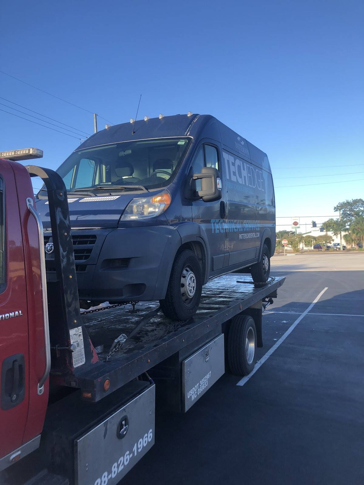 Red rollback carrying a dark blue high-roof cargo van in a parking lot